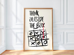 Framed poster with 'Think Outside The Box' text and a tic-tac-toe board on a white wall.