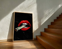 Framed artwork of red lips with a cigarette on a black background, leaning against a wall next to wooden stairs.