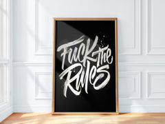 Framed poster with 'Fuck the Rules' text on a black background in a room with white walls and wooden floor.