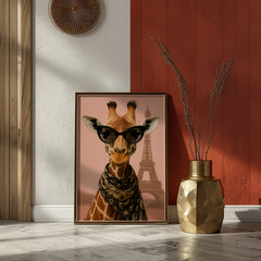 Framed artwork of a giraffe wearing sunglasses with the Eiffel Tower in the background, placed on a floor against a wall.