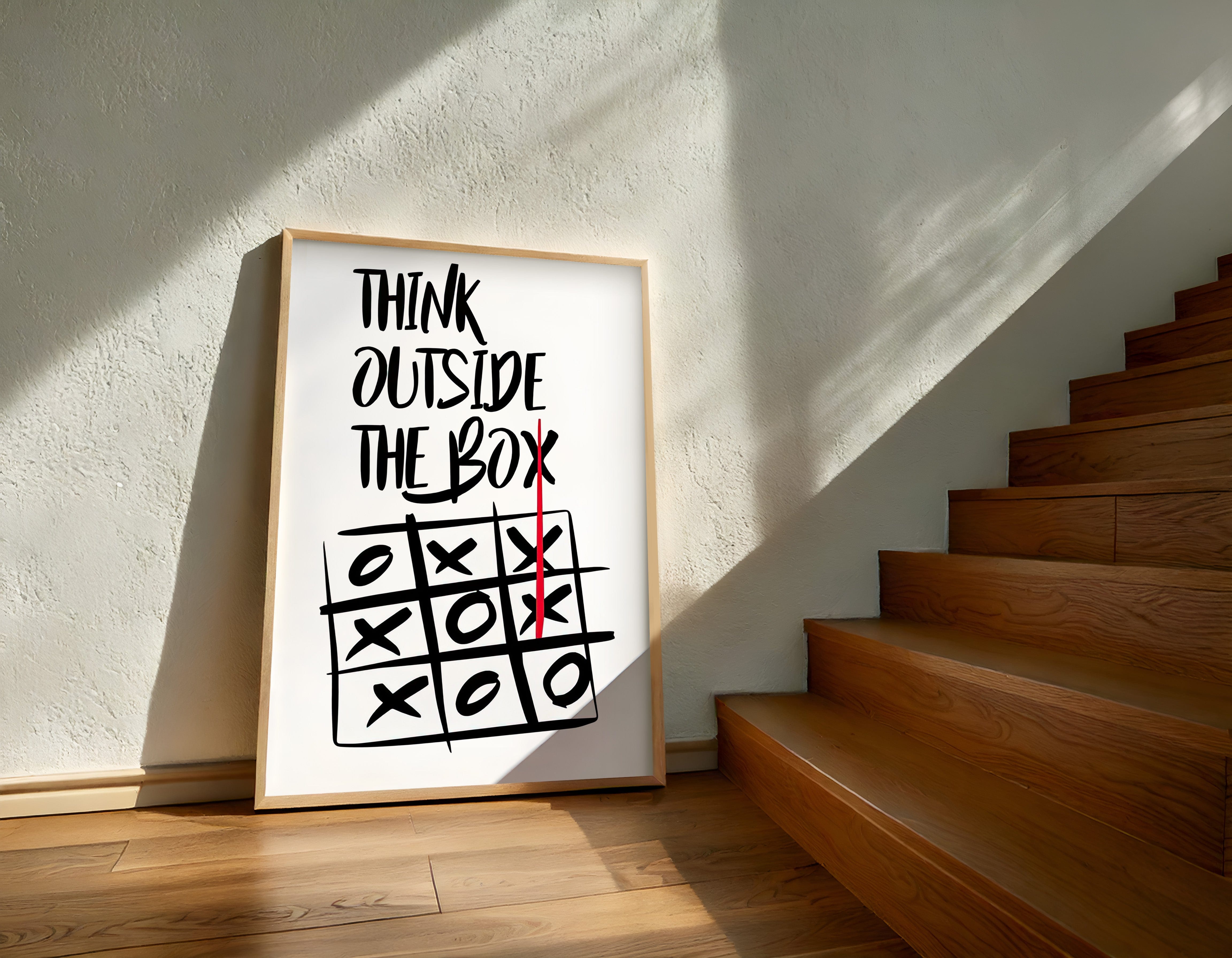 Framed poster with 'Think Outside The Box' quote on a wall next to wooden stairs