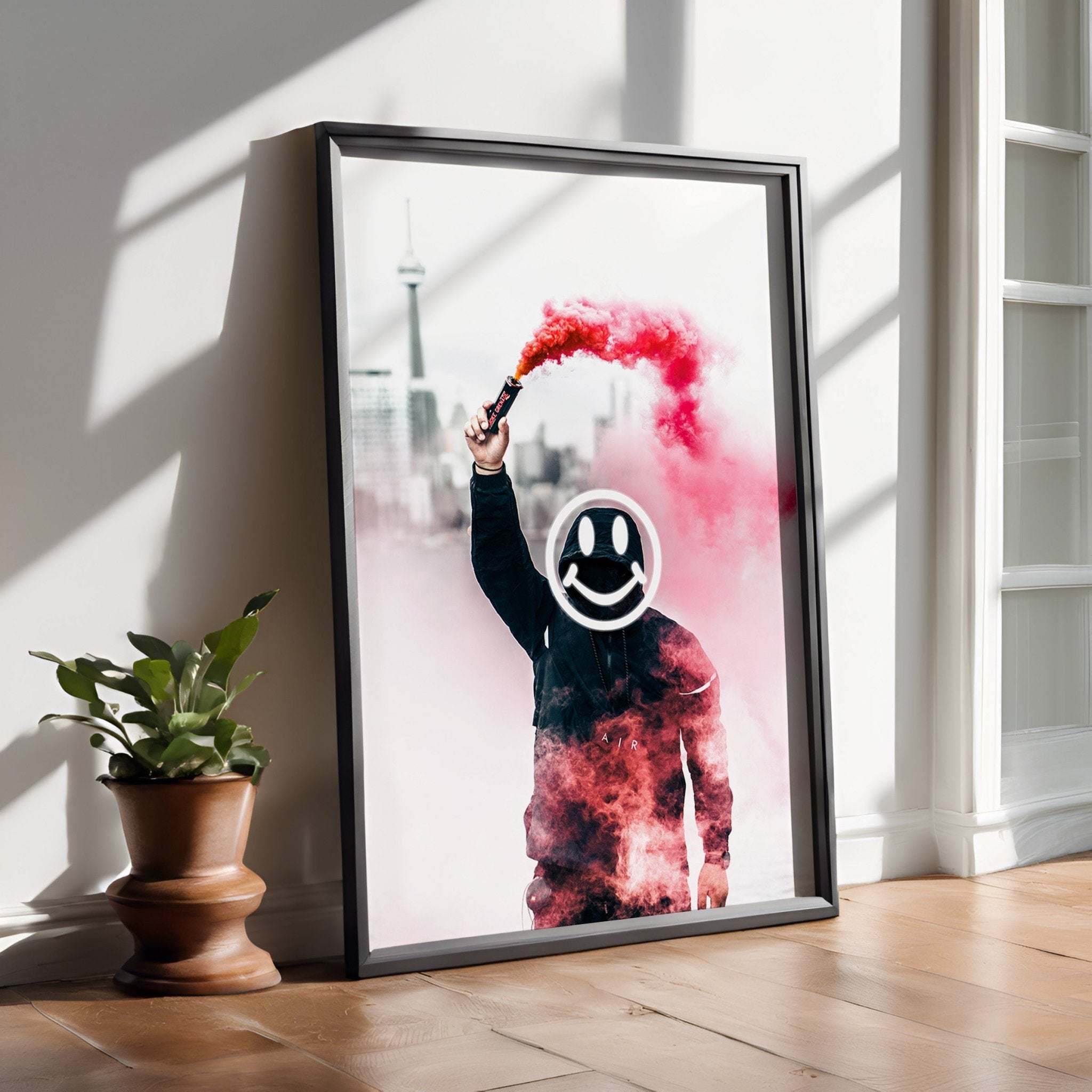 Framed artwork of a person holding a red smoke device with a smiley face symbol, placed on a wooden floor.