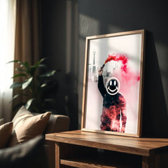 Framed artwork with a person holding a spray can and red smoke on a wooden table in a room.