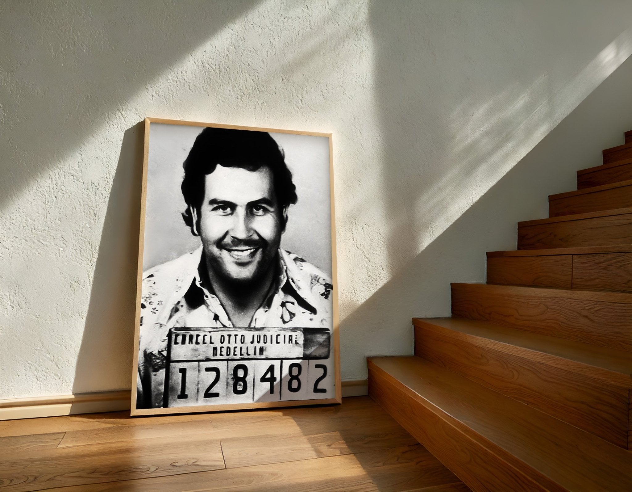 Framed black and white portrait of a man with a smile on a wall next to wooden stairs.