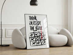 Framed poster with 'Think Outside The Box' quote and tic-tac-toe game in a modern living room.