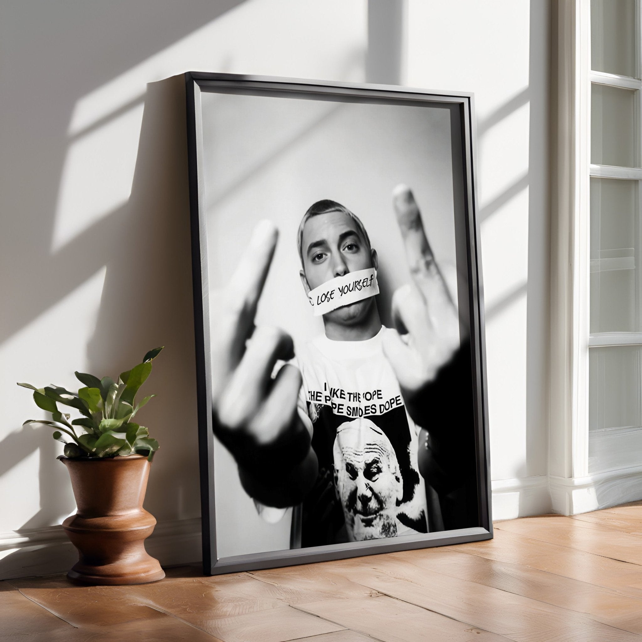 Framed black and white portrait of a person with a plant on a wooden floor.
