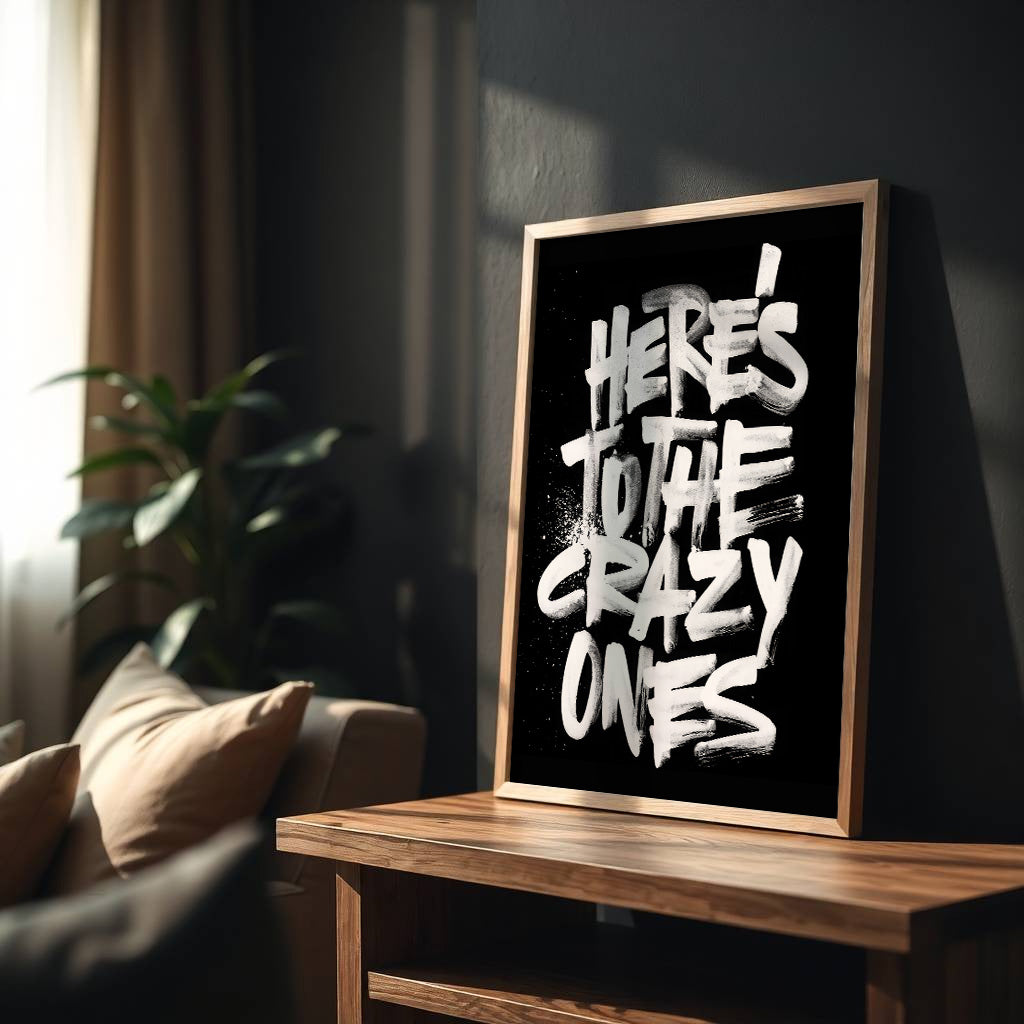 Framed artwork with 'Here's to the crazy ones' text on a wooden table in a living room.
