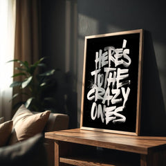 Framed artwork with 'Here's to the crazy ones' text on a wooden table in a living room.